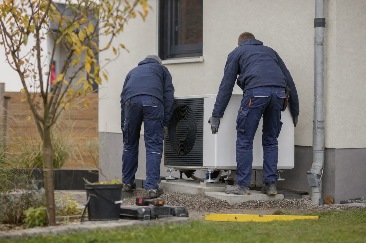 Monteure setzen die Außeneinheit einer Wärmepumpe auf das Fundament